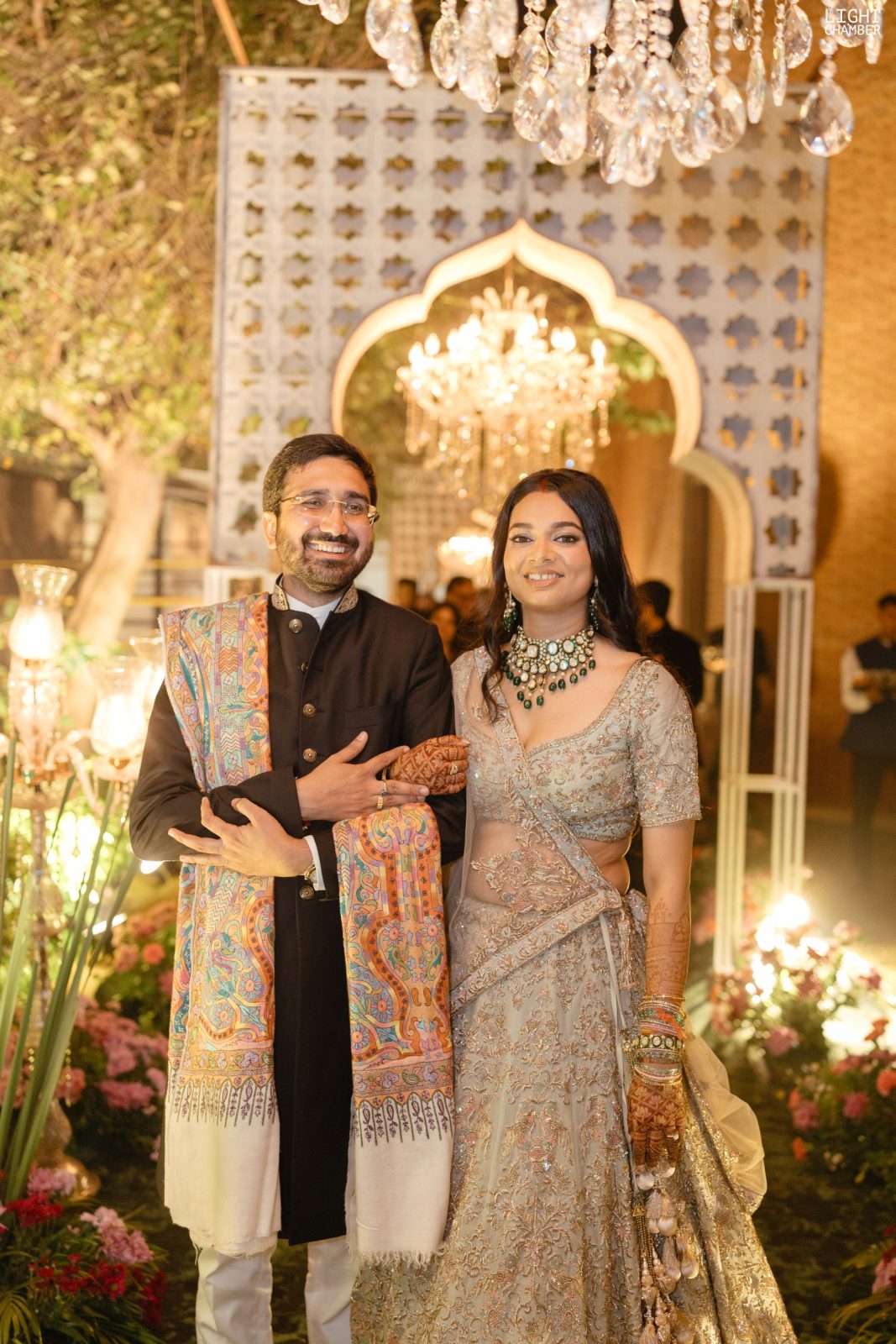 A built décor installation — floral archways, a candlelit lounge and hanging crystal