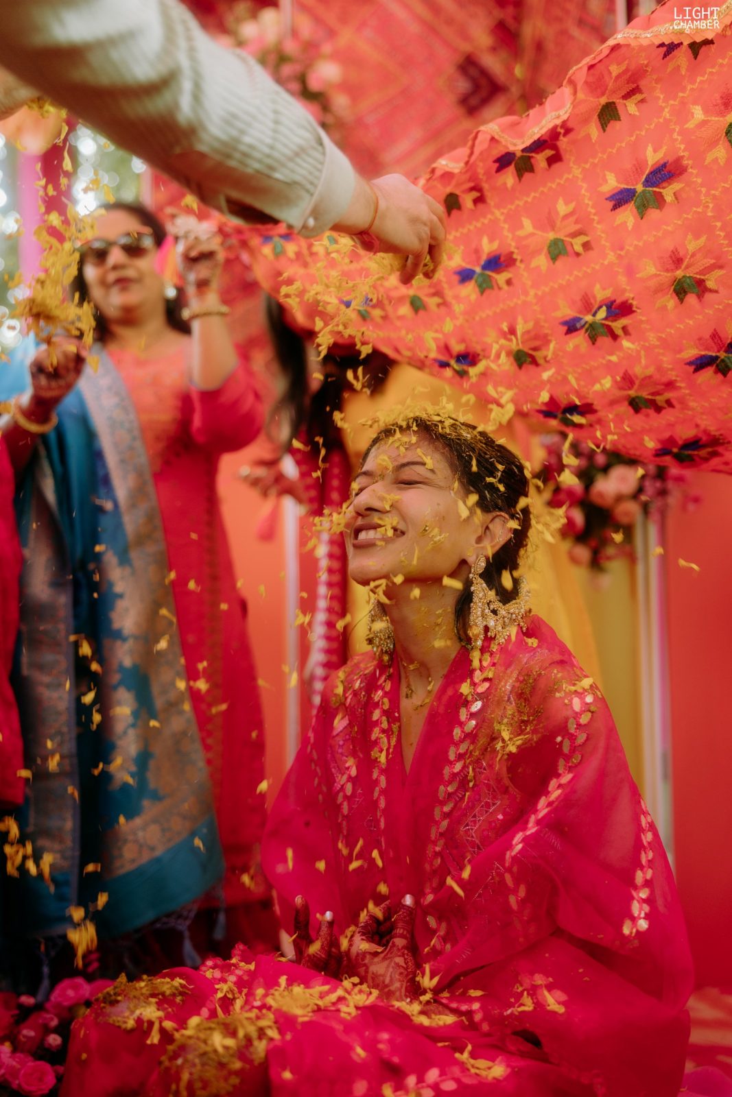 Haldi under a canopy of pink and marigold, turmeric and petals in the air