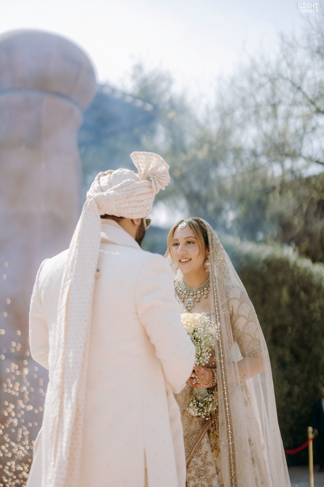 The couple at the mandap under a petal shower, garlanded and framed by florals