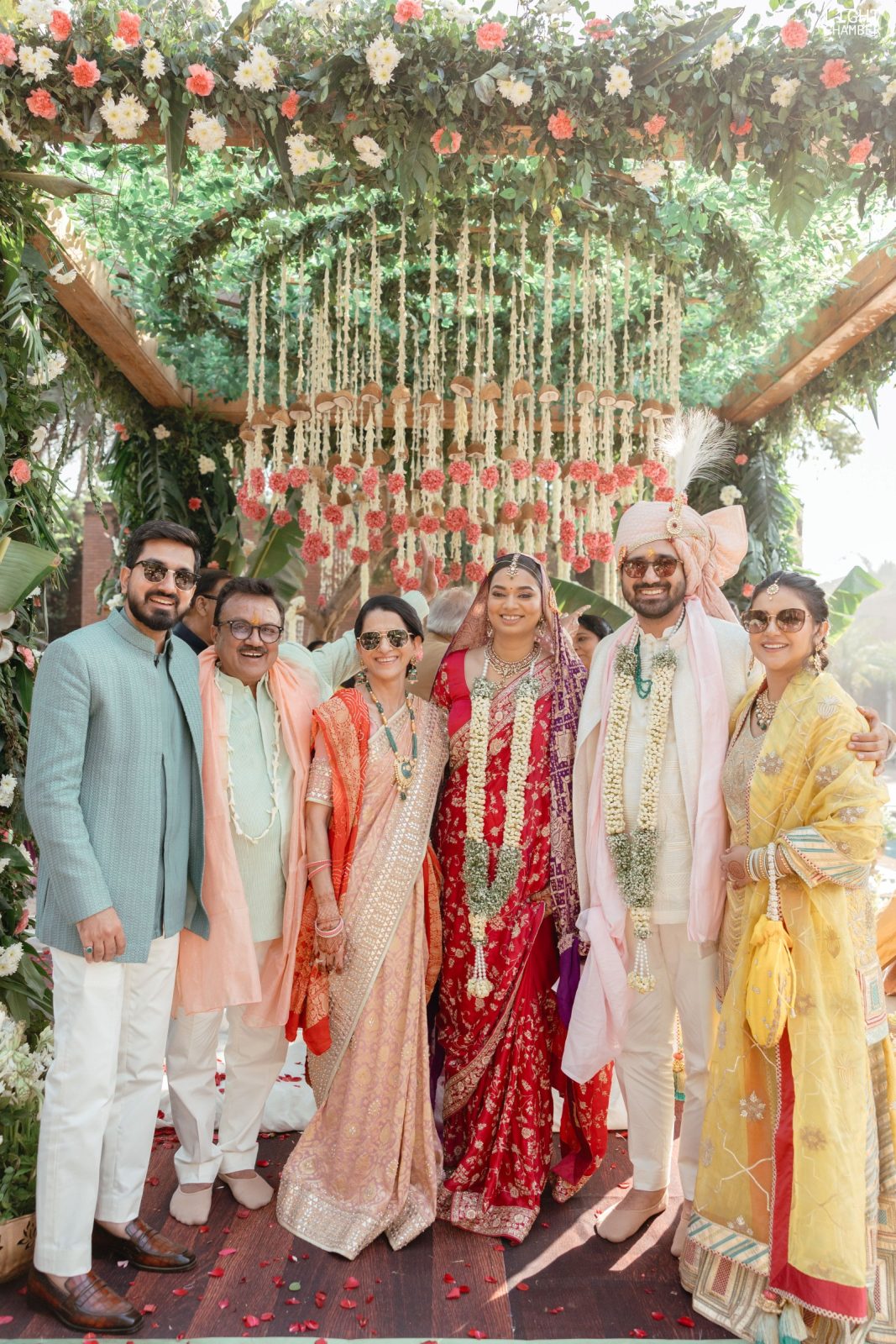 The couple at the mandap under a petal shower, garlanded and framed by florals