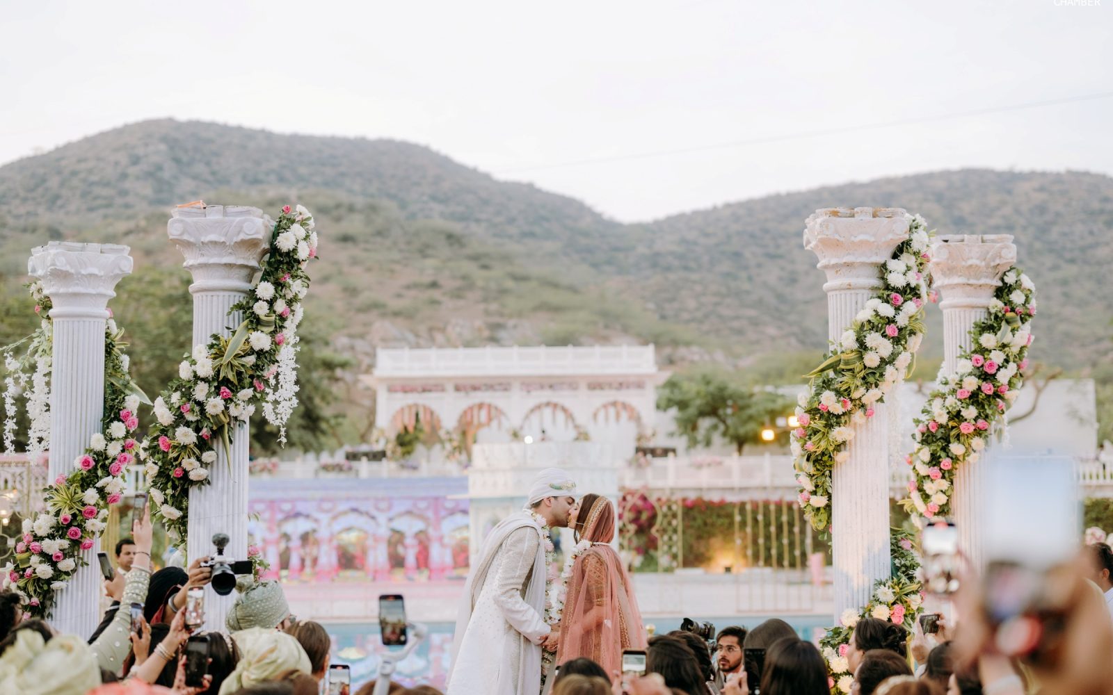 A Rajasthan palace dressed for a wedding — sandstone courtyards, lit façades and a mandap set against the hills