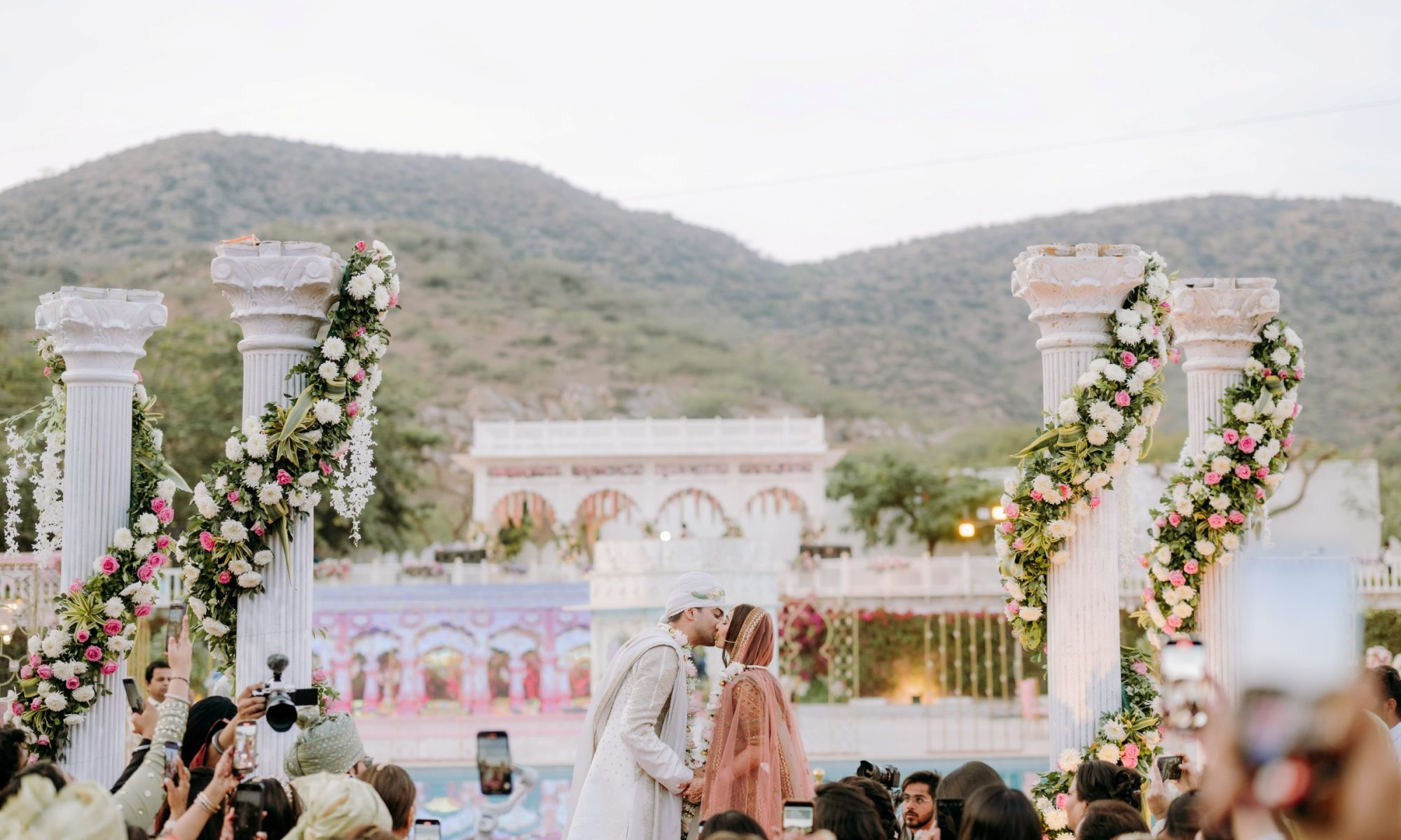 A Rajasthan palace dressed for a wedding — sandstone courtyards, lit façades and a mandap set against the hills
