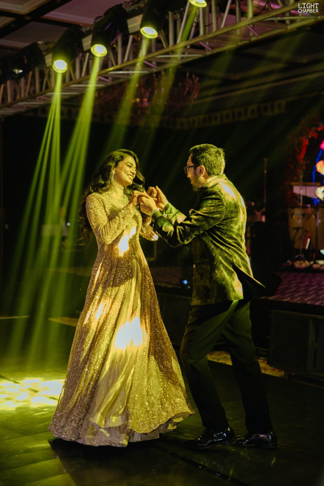 A sangeet stage lit for performance, guests dancing against an arched backdrop